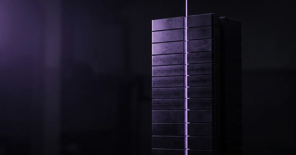 Columna vertical de bloques oscuros apilados en capas, con una línea de luz púrpura que la divide, sobre fondo oscuro